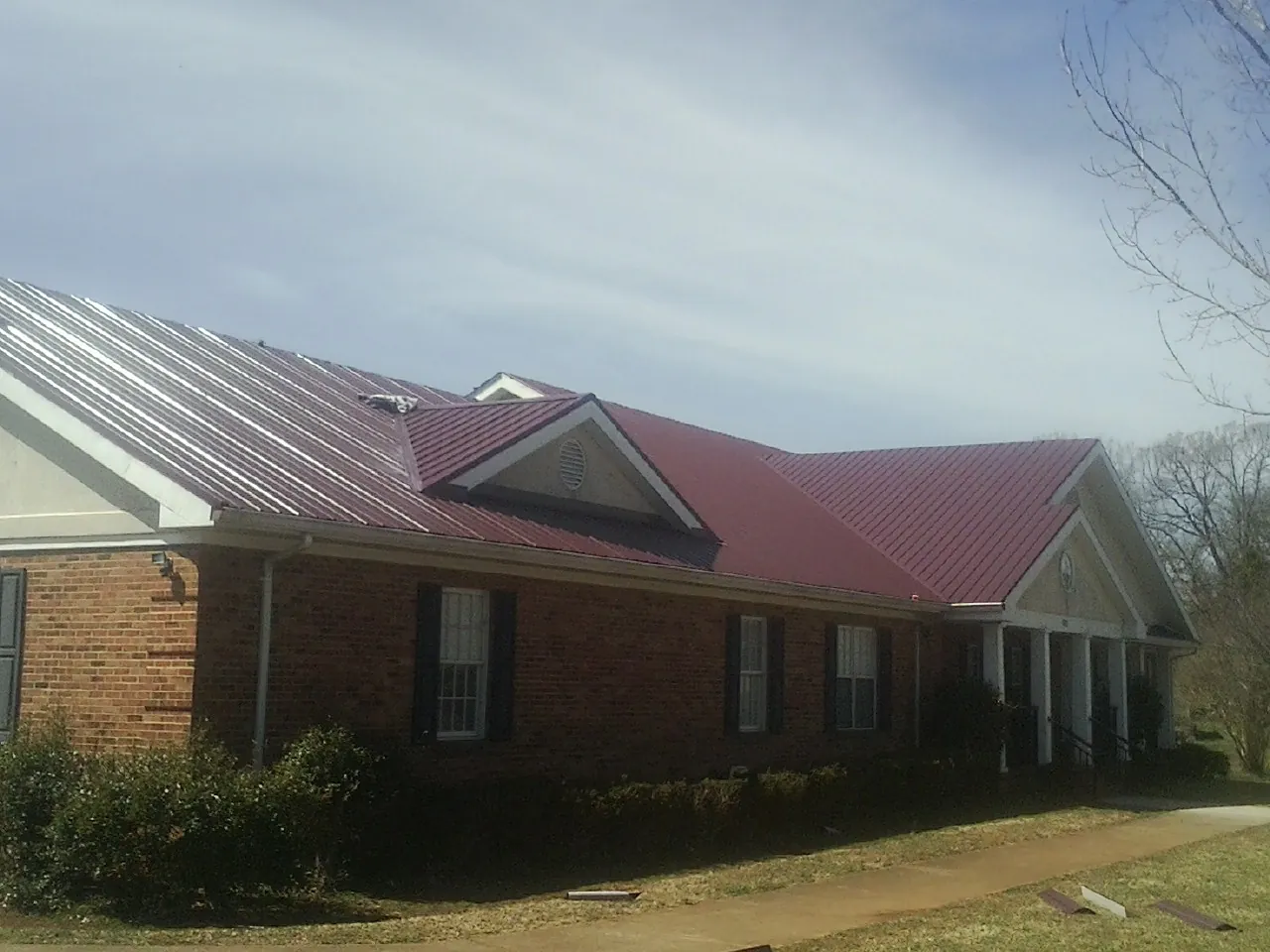 Red metal roof with gabled entries on a long brick building, from a Hail Damage Roof Repair job in Wells Tannery