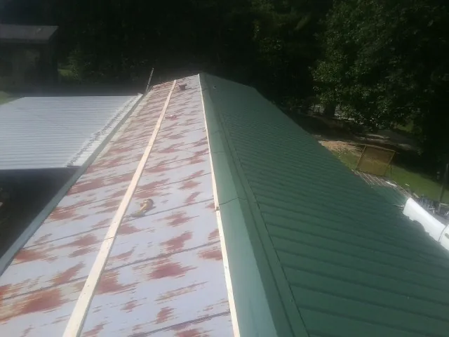 Old rusted panels beside newly installed green metal roofing — Wind Damage Roof Repair by Roofing Brothers in Wells Tannery