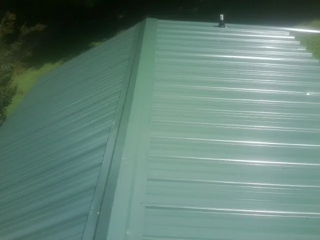 New green metal panels meeting at the ridge of a roof — Flat Roof Repair work by our crew in Wells Tannery