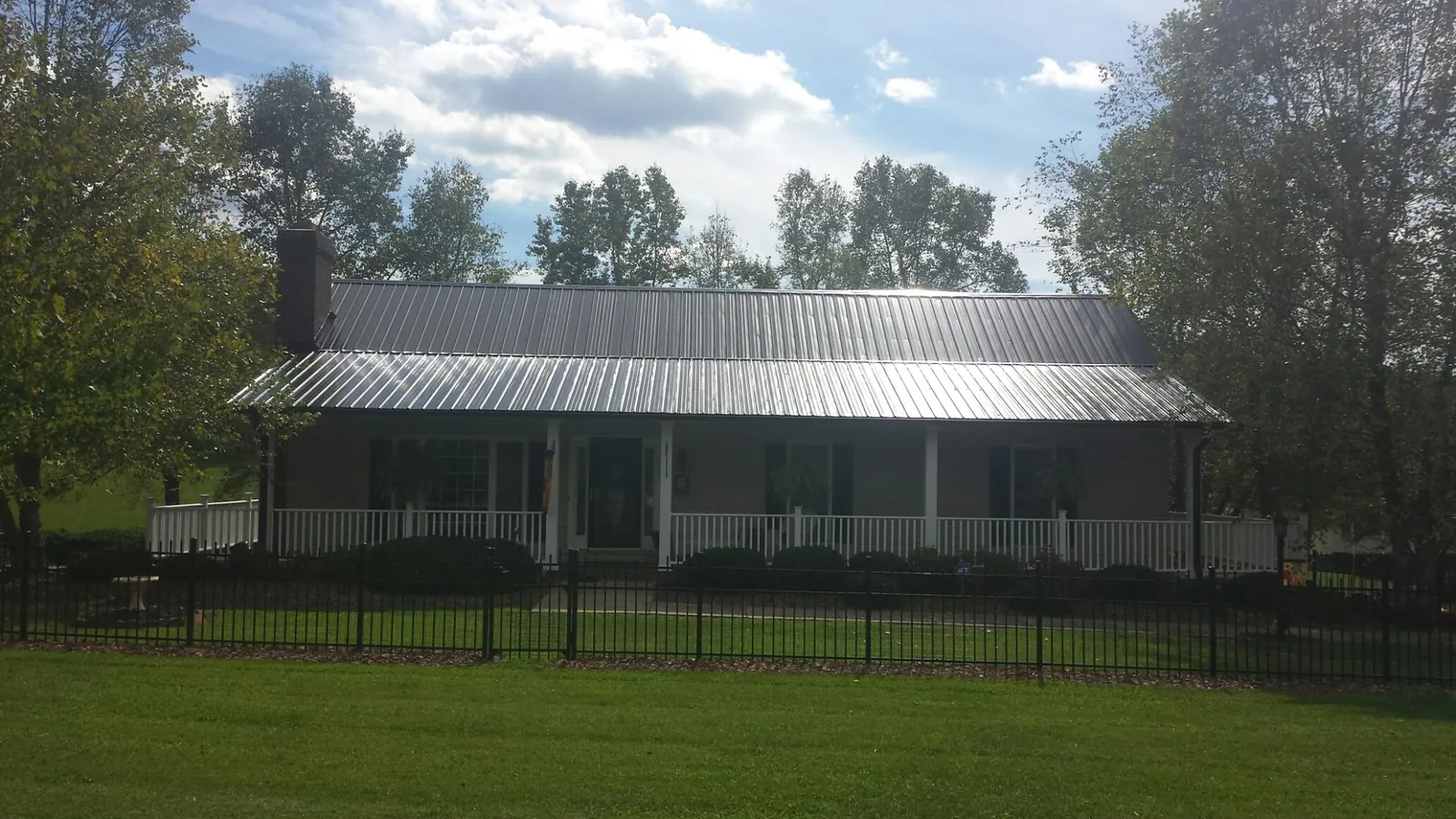 Gray metal roof on a brick ranch with a full width front porch — Gutter Guard Installation work by our crew in Wells Tannery
