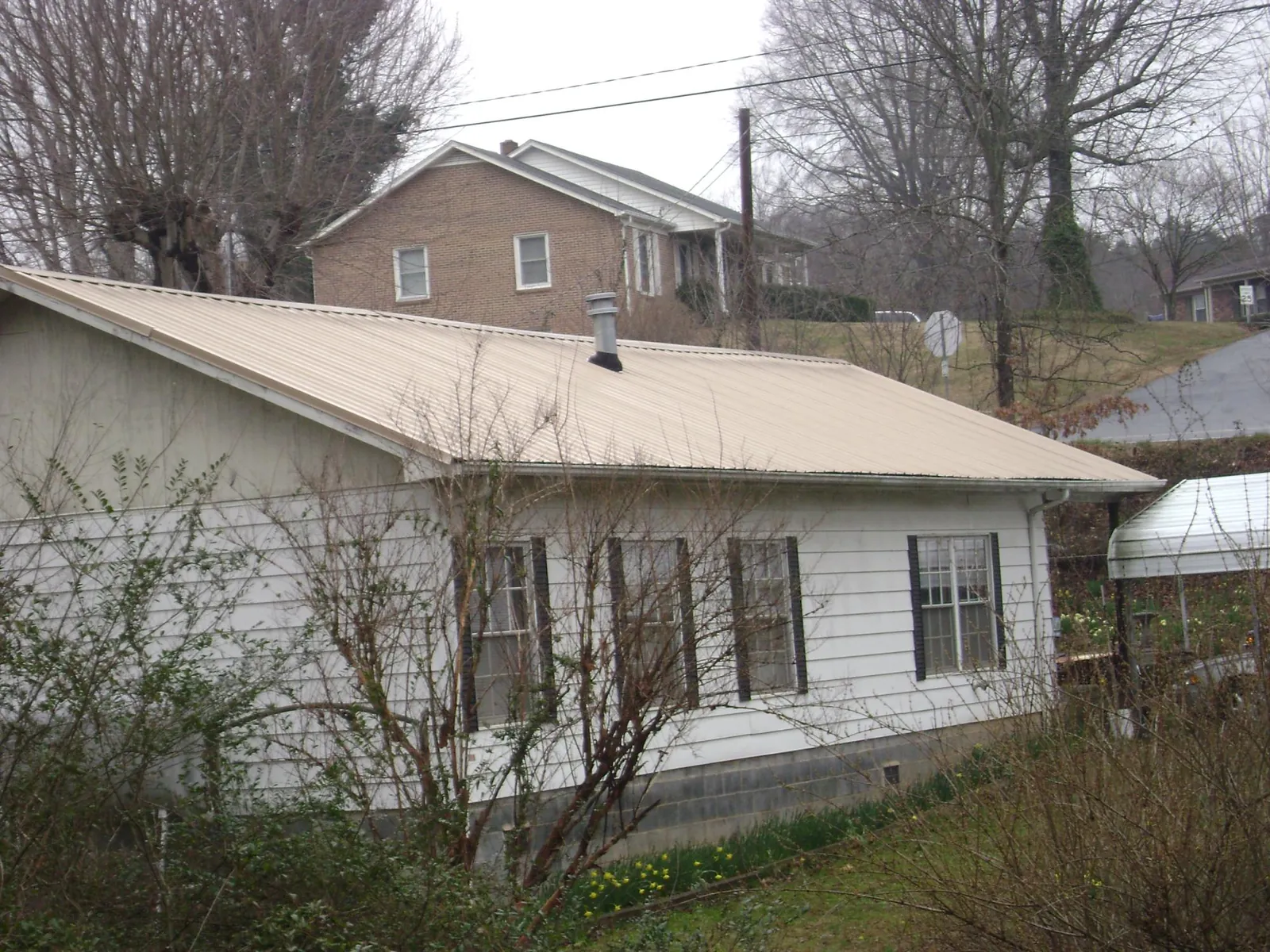Tan metal roof on a white sided house set into a hillside — Commercial Roofing by Roofing Brothers in Wells Tannery